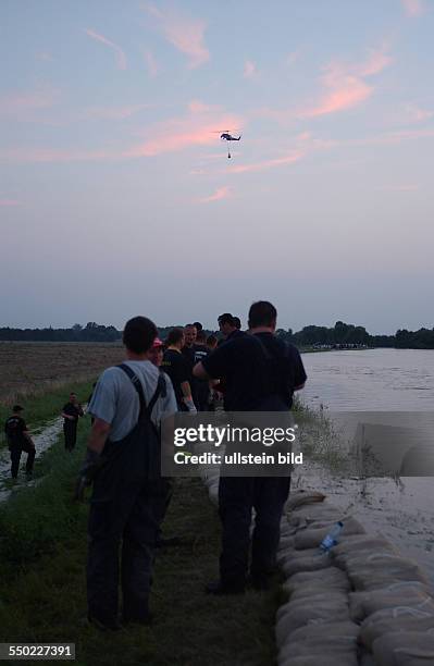 Feuerwehrleute warten auf einer durchweichten Deichkrone bei Mildensee auf Sandäcke die von einem Bundeswehrhubschrauber herbeigeflogen werden