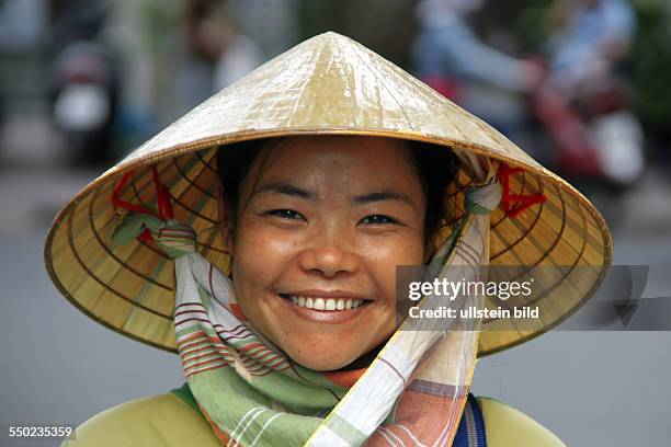 VIETNAMESIN MIT REISHUT EINEM NON LA. EIN FLACHER KEGELHUT AUS HELLEM FLECHTWERK, DER IN WEITEN TEILEN SÜDOSTASIENS, VORZUGSWEISE IN VIETNAM