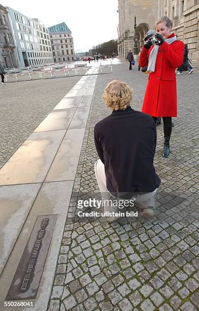Touristen fotografieren sich an der Hinweistafel zur Erinnerung an den Verlauf der Berliner Mauer in Berlin-Mitte