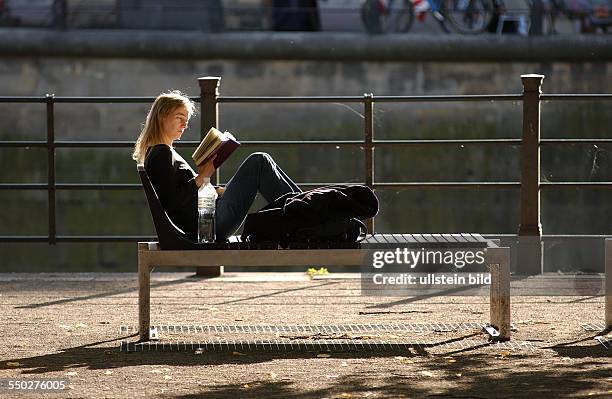 Junge Frau liest am Spreeufer in Berlin