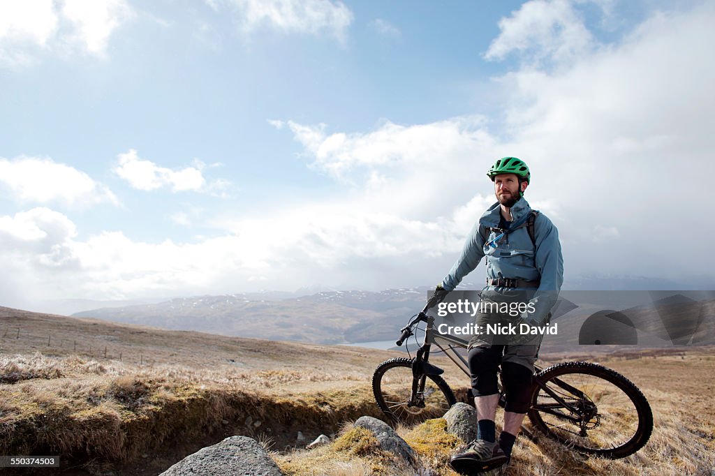 A mountain biker stop to rest looking across a beautiful Scottish landscape