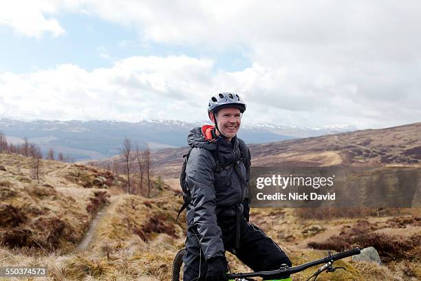a cheerful mountain biker on a bike trail with the scottish highlands in the background - protective sportswear stock-fotos und bilder