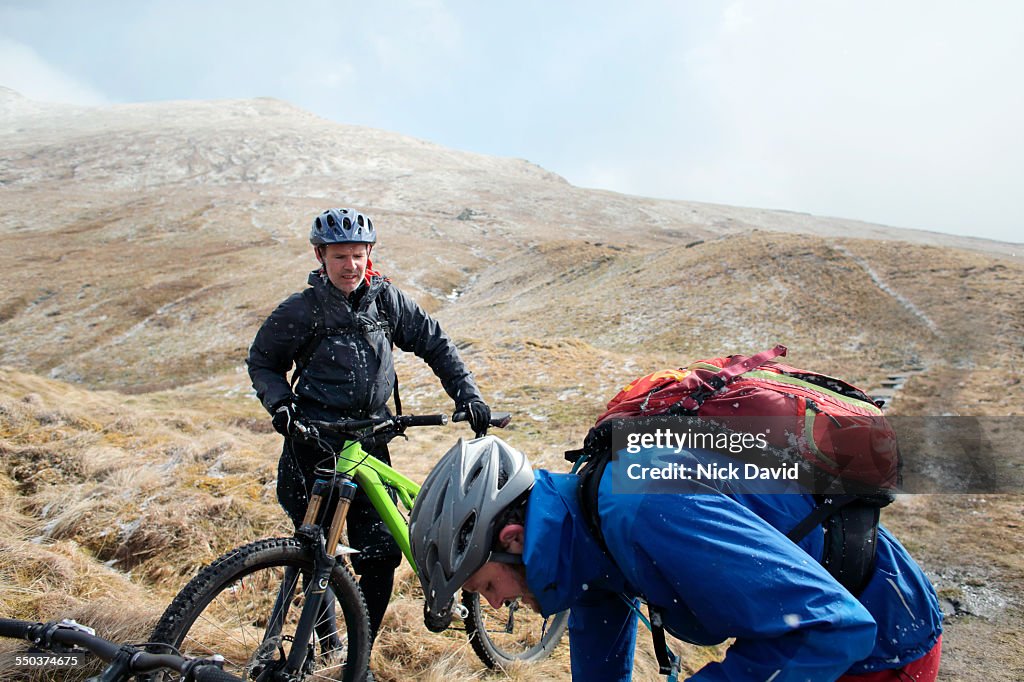 Two male mountain bikers stop to make adjustments to their bikes in the Highlands of Scotland