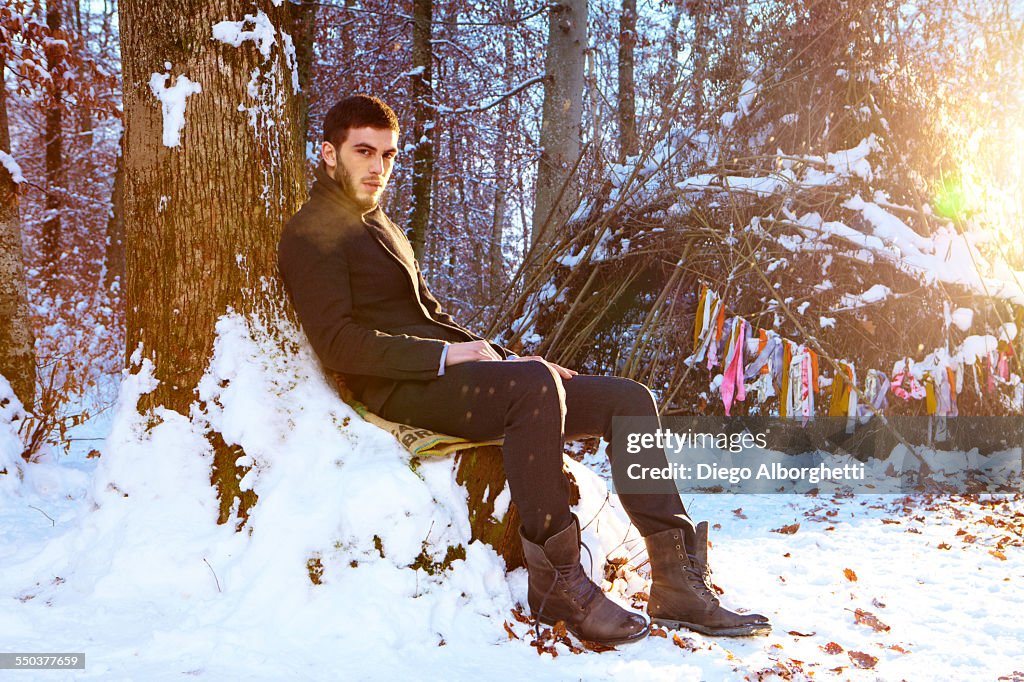 Man sitting beside a tree in snow-covered forest