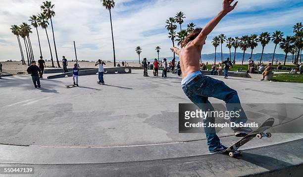 Skateboarder with no shirt, arms raised, and pants sagging, off the side of a ramp. Los Angeles, California.