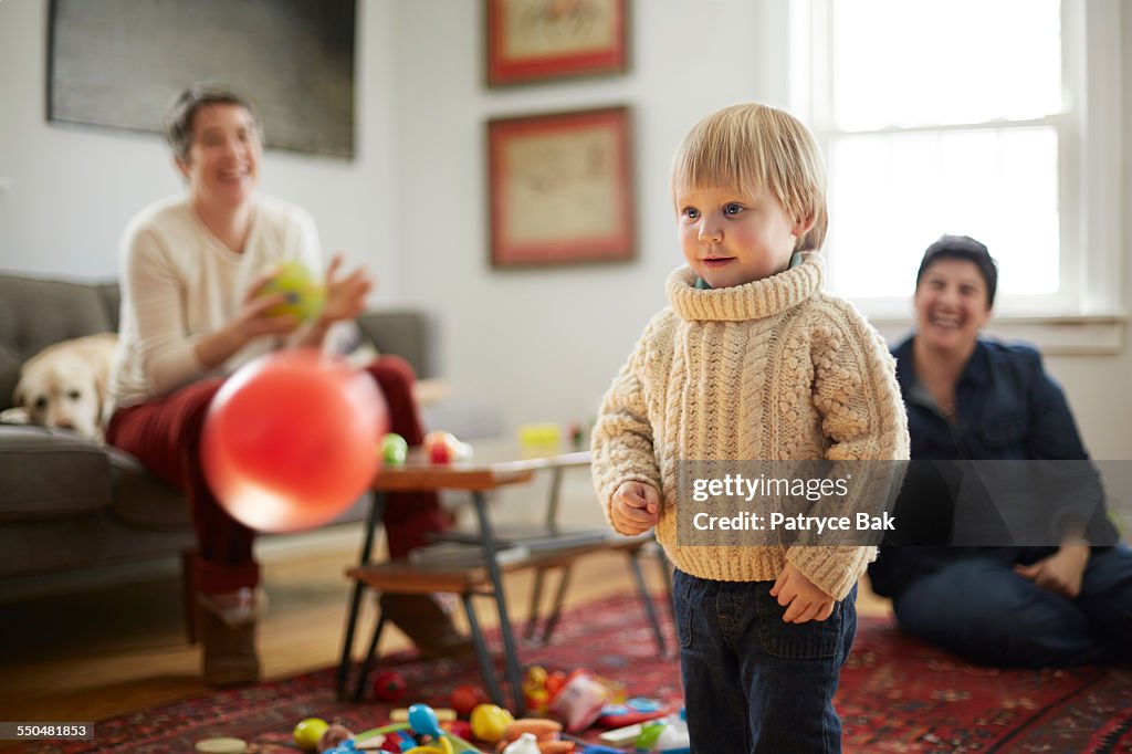 Lesbian moms & daughter play catch in living room