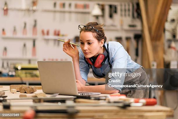 young carpenter in wood workshop using labtop - timmerman stockfoto's en -beelden