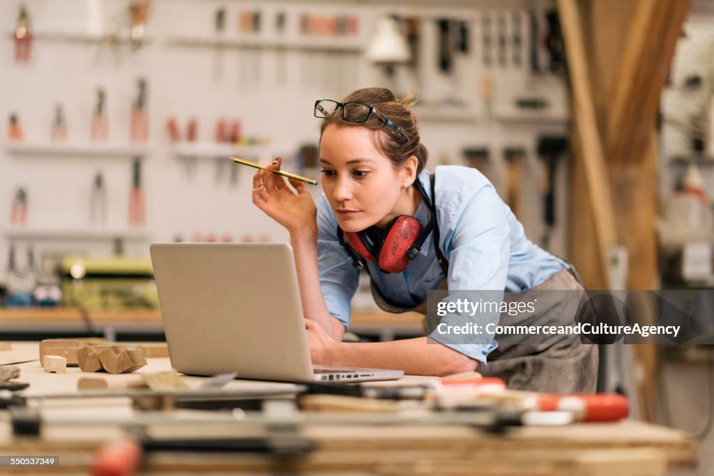 Young carpenter in wood workshop using labtop