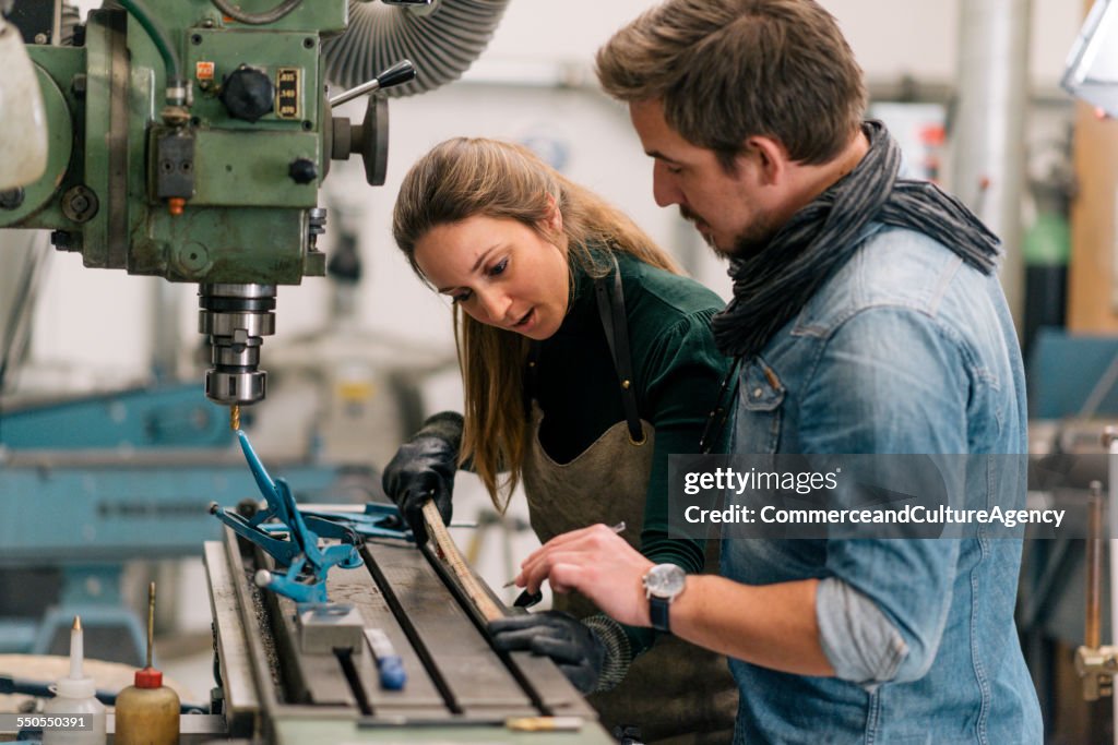 Craftswoman and man in metal workshop measuring