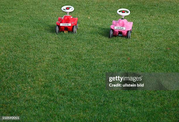 Zwei Bobbycars auf einer Wiese.