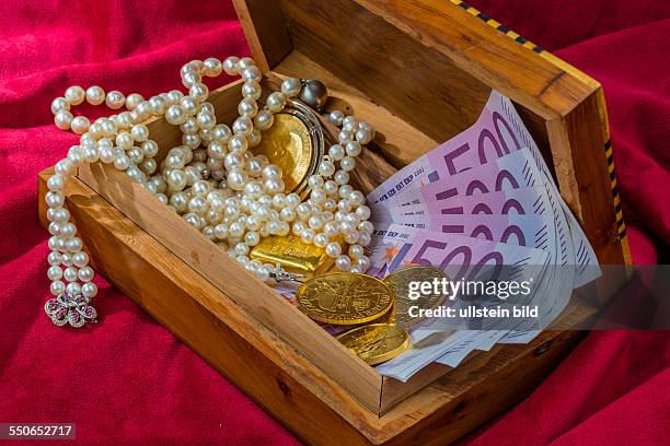 Gold in Münzen und Barren mit Schmuck auf rotem Samt. Symbolfoto für Reichtum, Luxus, Reichensteuer.