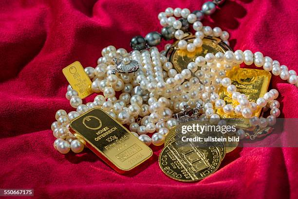 Gold in Münzen und Barren mit Schmuck auf rotem Samt. Symbolfoto für Reichtum, Luxus, Reichensteuer.