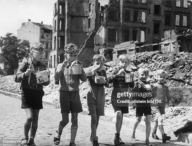 Food supply in Berlin after the war: Boys eating their school lunch from tin cans in ther streets, in the background ruins and rubble