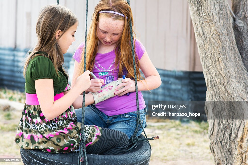 Girl signing a cast on swing.