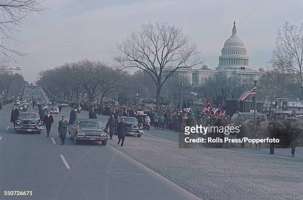 President of the United States, Lyndon B. Johnson surrounded by Secret Service agents, rides in a presidential limousine from the Capitol building to...