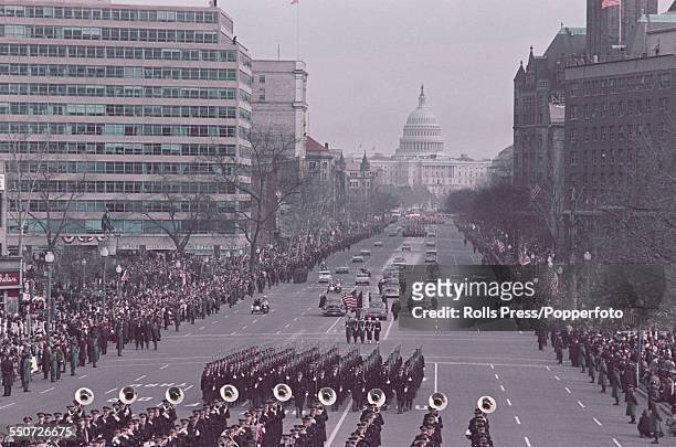 President of the United States, Lyndon B. Johnson surrounded by Secret Service agents and a military escort, rides in a presidential limousine from...