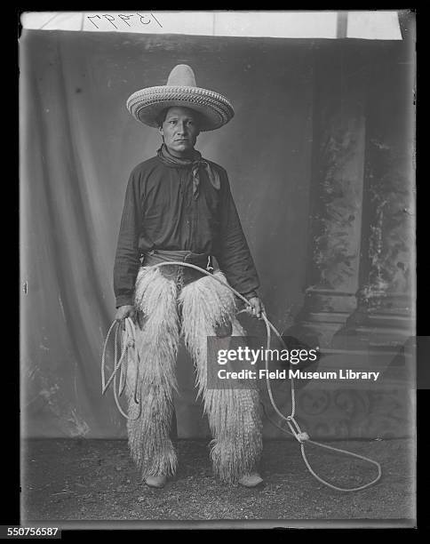 Portrait of Native American Oglala Sioux Ivan Star Comes Out, wearing cowboy clothing, sheepskin chaps, tall cowboy hat, and carrying a lariat at the...