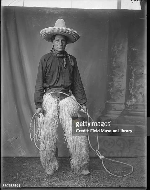Portrait of Native American Oglala Sioux Ivan Star Comes Out, wearing cowboy clothing, sheepskin chaps, tall cowboy hat, and carrying a lariat at the...