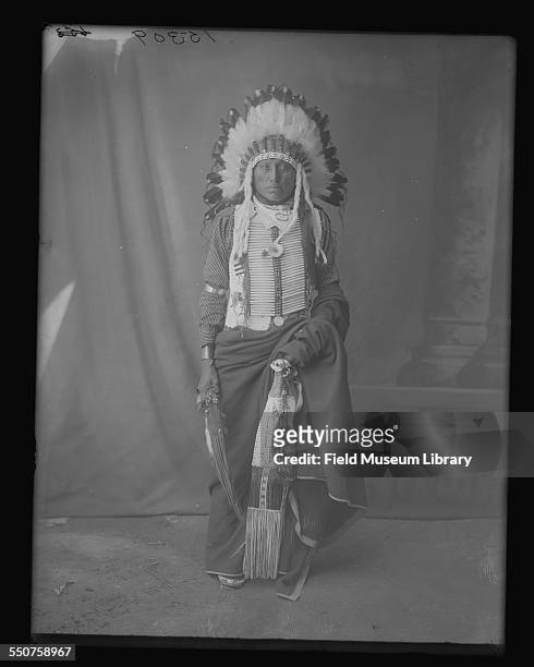 Portrait of Black Tail Deer, a Native American Rosebud Sioux wearing a feather headdress, a hair pipe breastplate and beaded vest, beaded moccasins...