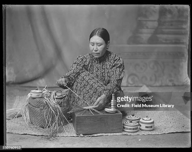 Portrait of a First Nations Nuu-chah-nulth woman identified as Annie Williams, daughter of Chief Atlieu of the Nootka, as she weaves baskets at the...