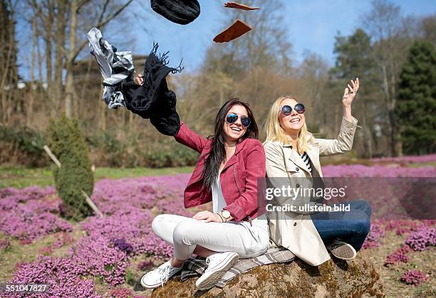 Frühlingshafte Temperaturen und Sonne, Zwei junge Frauen werfen Winterbekleidung wie Handschuhe, Mütze und Schal symbolisch weg