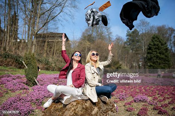 Frühlingshafte Temperaturen und Sonne, Zwei junge Frauen werfen Winterbekleidung wie Handschuhe, Mütze und Schal symbolisch weg