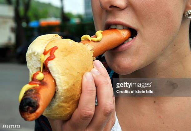 Junge Frau isst Rostwurst mit Senf und Ketchup im Brötchen