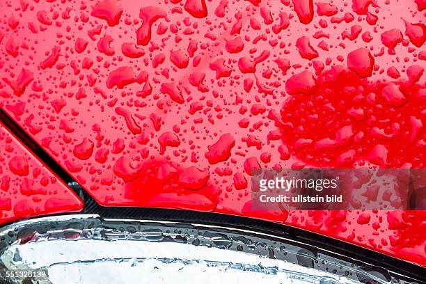 Nach einem Regen perlen Regentropfen auf dem Lack eines Autos ab. Wassertropfen auf rotem Hintergrund