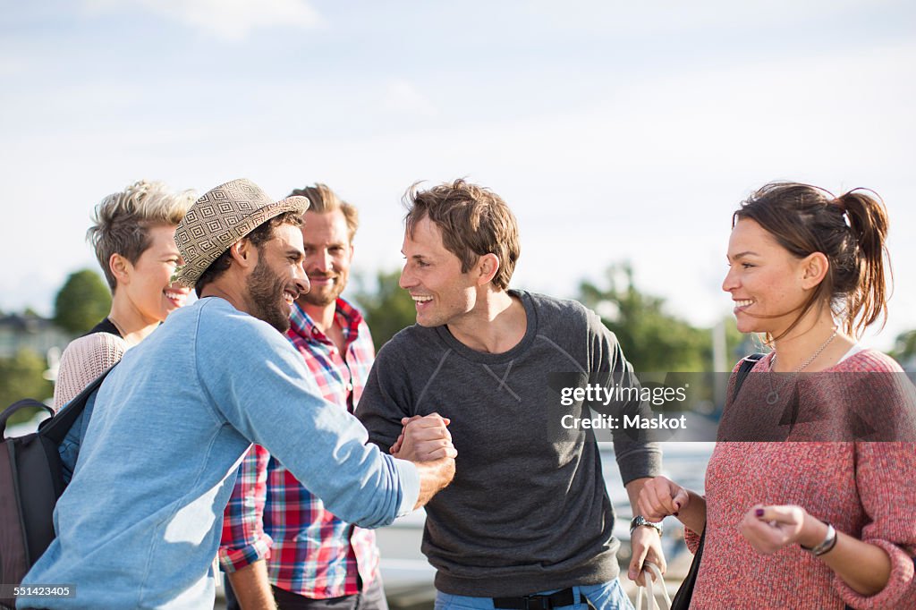 Happy friends greeting each other against sky