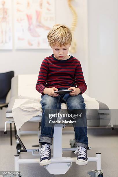 boy using smart phone on examination table in orthopedic clinic - examination table stock pictures, royalty-free photos & images