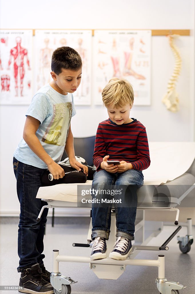 Brothers using smart phone at examination table in orthopedic clinic