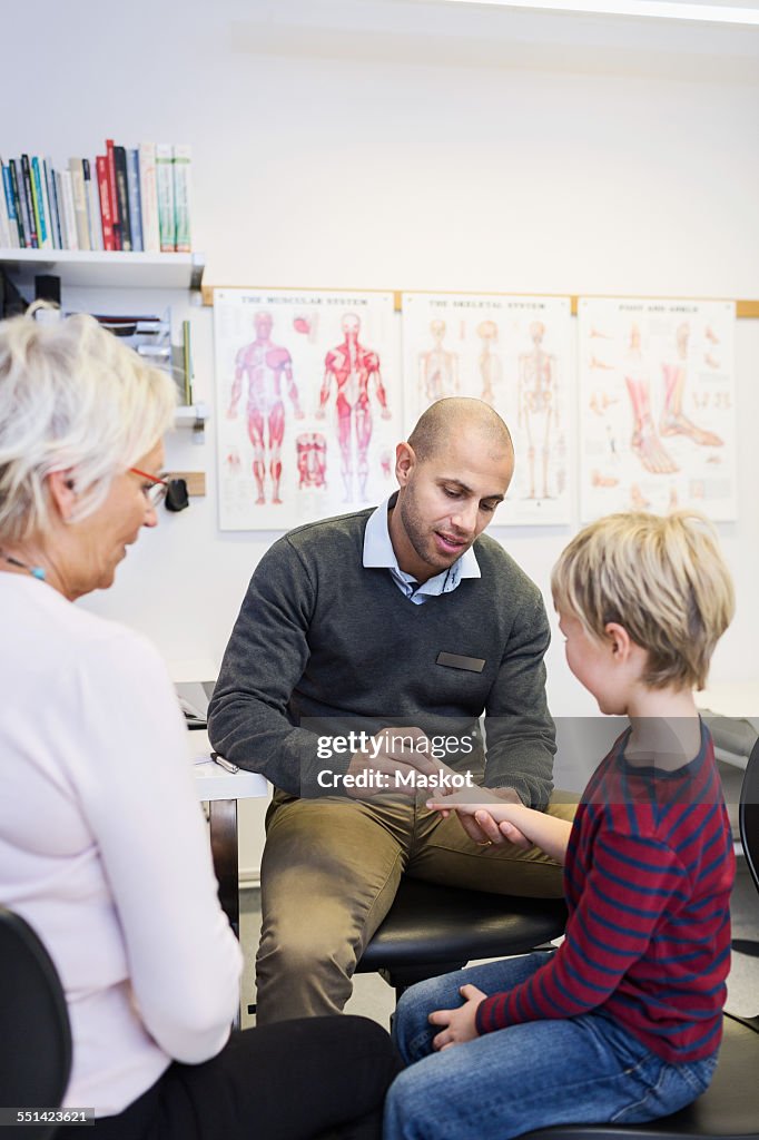 Grandmother looking at grandson being examined by orthopedic surgeon in clinic