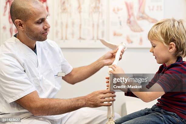male orthopedist explaining hand model to boy at clinic - orthopedic surgery stock pictures, royalty-free photos & images