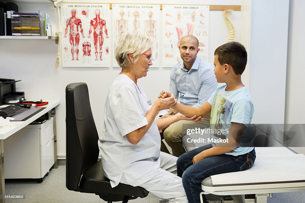 Father sitting by son being examined by orthopedic surgeon in clinic