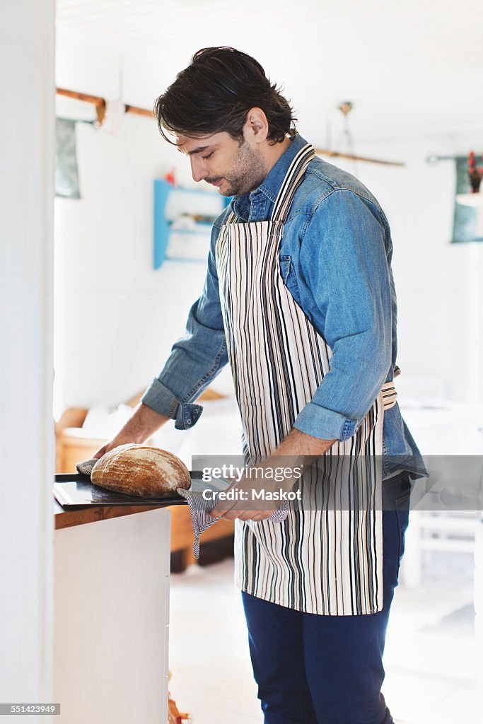 Side view of man holding freshly baked bread in tray at home