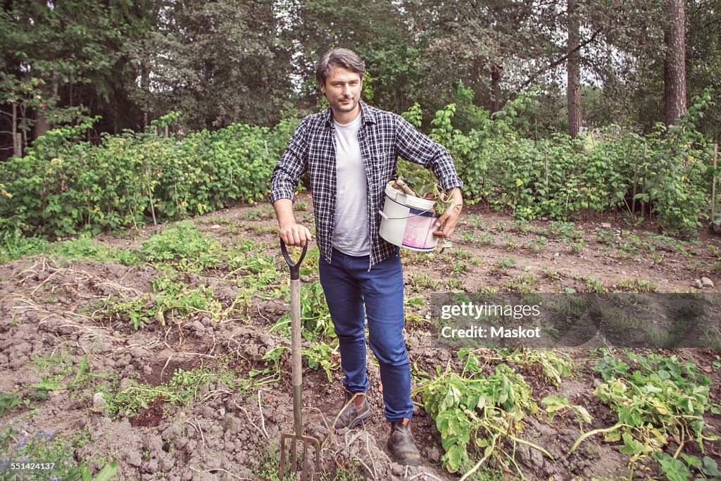 Full length portrait of confident man with gardening fork and bucket at organic farm