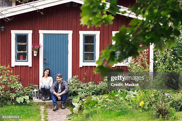mid adult couple sitting outside farmhouse - bauernhaus stock-fotos und bilder