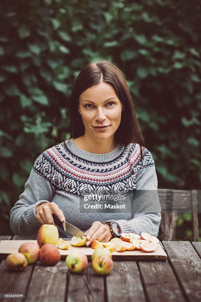 Portrait of mid adult woman cutting apples at table in organic farm