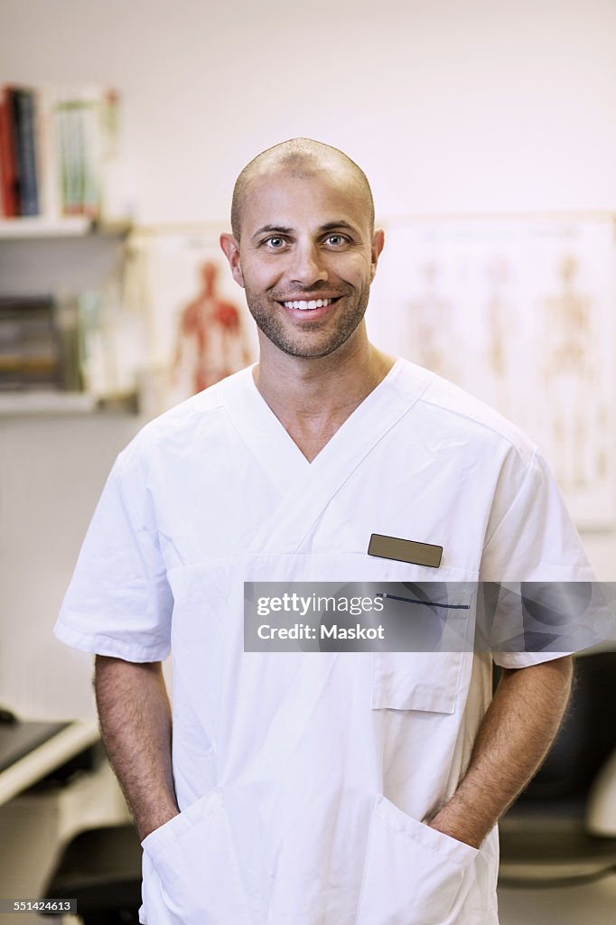 Portrait of smiling orthopedic surgeon standing with hands in pockets in clinic