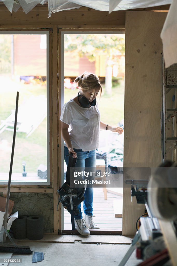 Full length of woman with tool belt entering in house being renovated