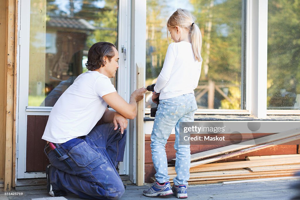 Father assisting girl in using cordless screwdriver on frame during home improvement