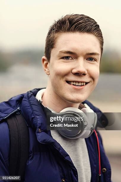 portrait of happy male university student with headphones around neck outdoors - headphone man on neck stockfoto's en -beelden