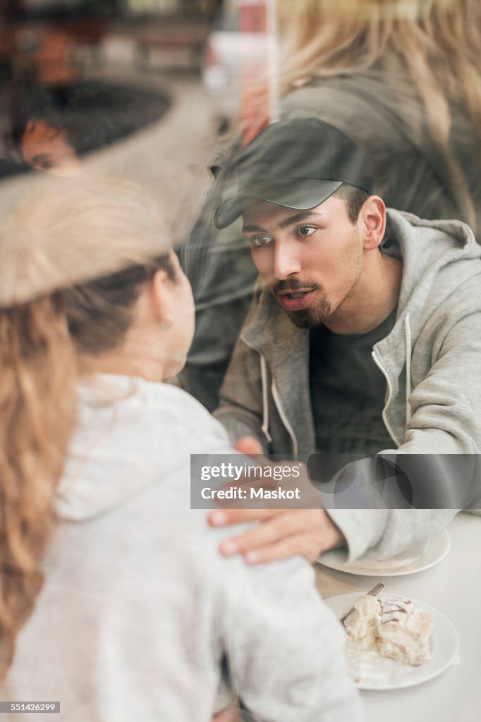 View of man consoling woman in cafe though glass