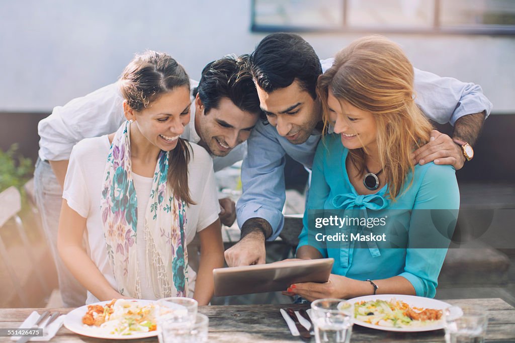 Group of four using digital tablet at outdoor cafe