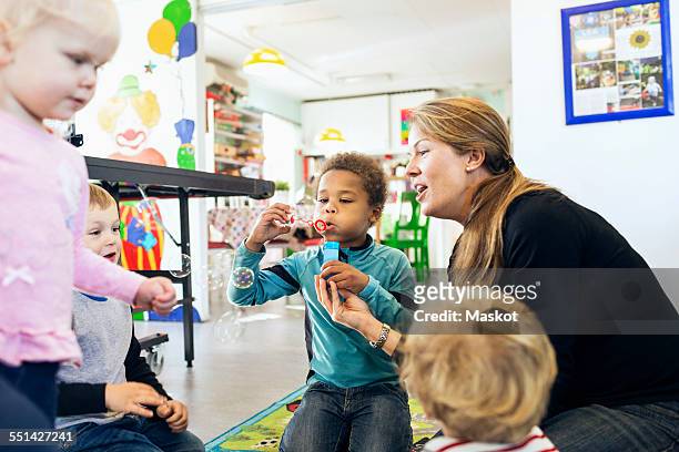 happy teacher and children playing with bubbles in kindergarten - nursery school building stock pictures, royalty-free photos & images