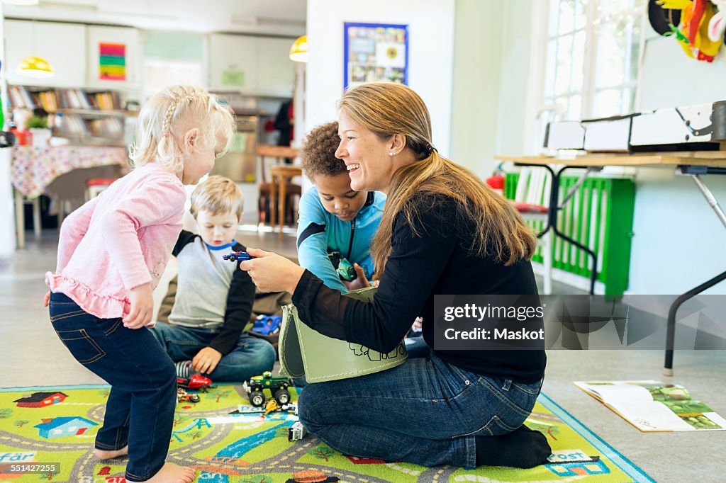 Full length of teacher giving toys to children