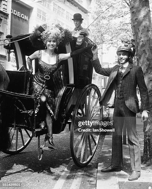 Portrait of actress Barbara Windsor being helped down from a hansom cab by musician Maurice Gibb, at a photocall for the musical 'Sing a Rude Song'...