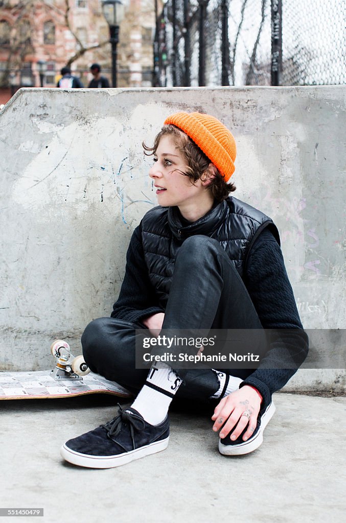 Young female skateboarder sitting in skate park