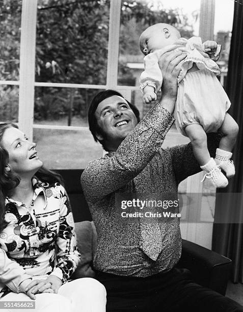 Irish broadcaster Terry Wogan with his wife Helen, holding his baby daughter Katherine in the air at their home, circa 1972.