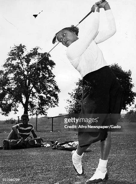 Woman wearing plus fours taking a golf swing, with a young boy watching her, Washington DC, 1938.